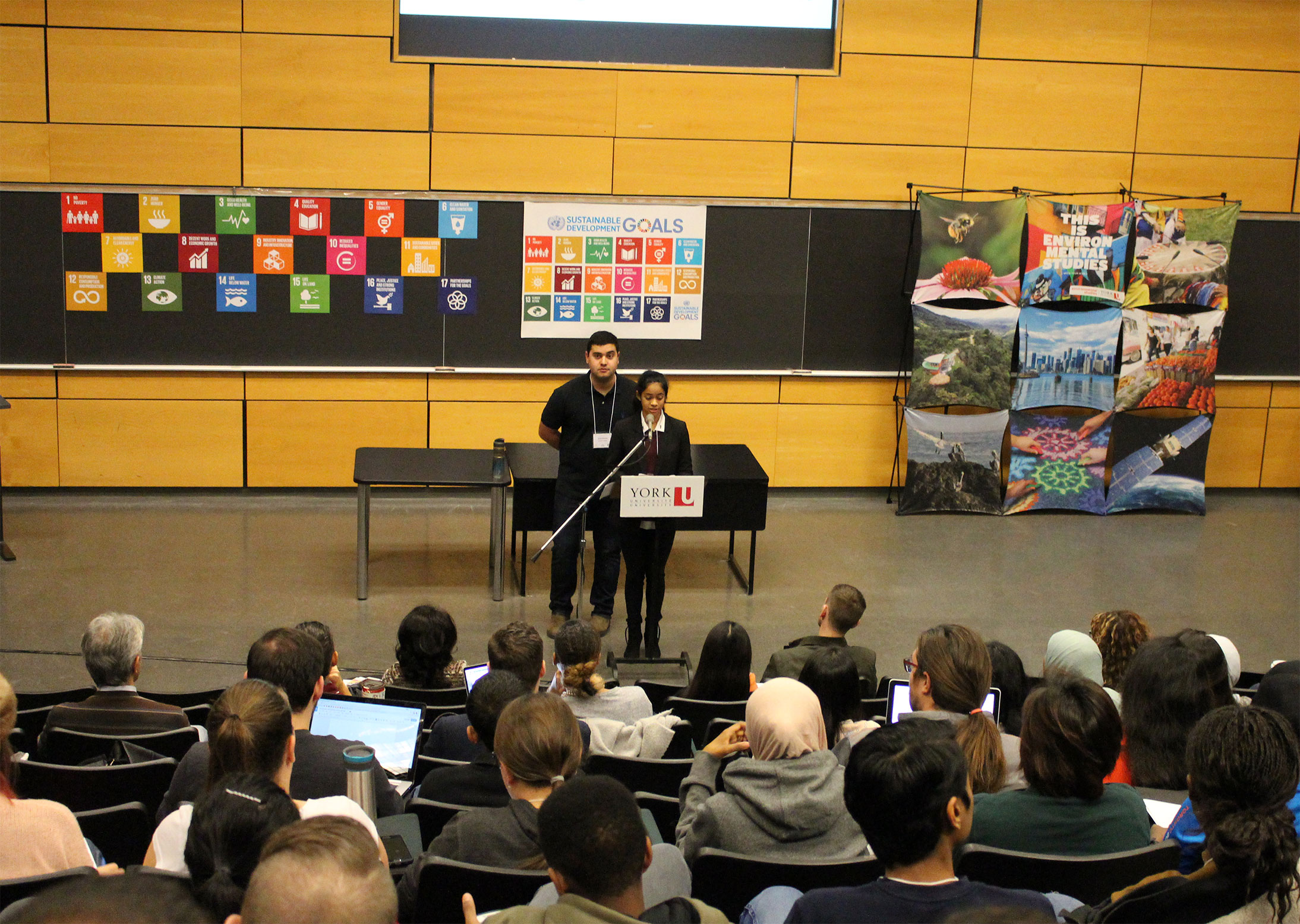 This is a picture of Aliya and Joey addressing a large lecture hall at the United Nations Sustainability Development Goals training.