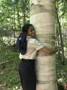 Aliya hugging a birch tree in her Ontario Parks Ranger uniform.